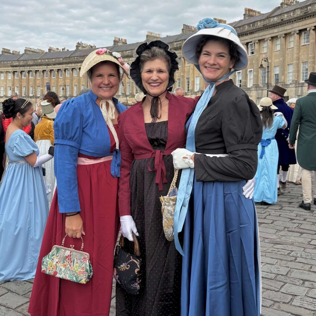 Three women in Regency dresses posing in front of the Royal Crescent in Bath